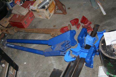1992 Ford Bronco - Various automotive parts, including a blue hydraulic jack and a rusty exhaust system, are laid out on a garage floor.