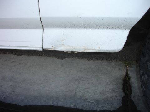 1996 Ford Bronco - Close-up of a white vehicle's lower body panel showing damage and rust.