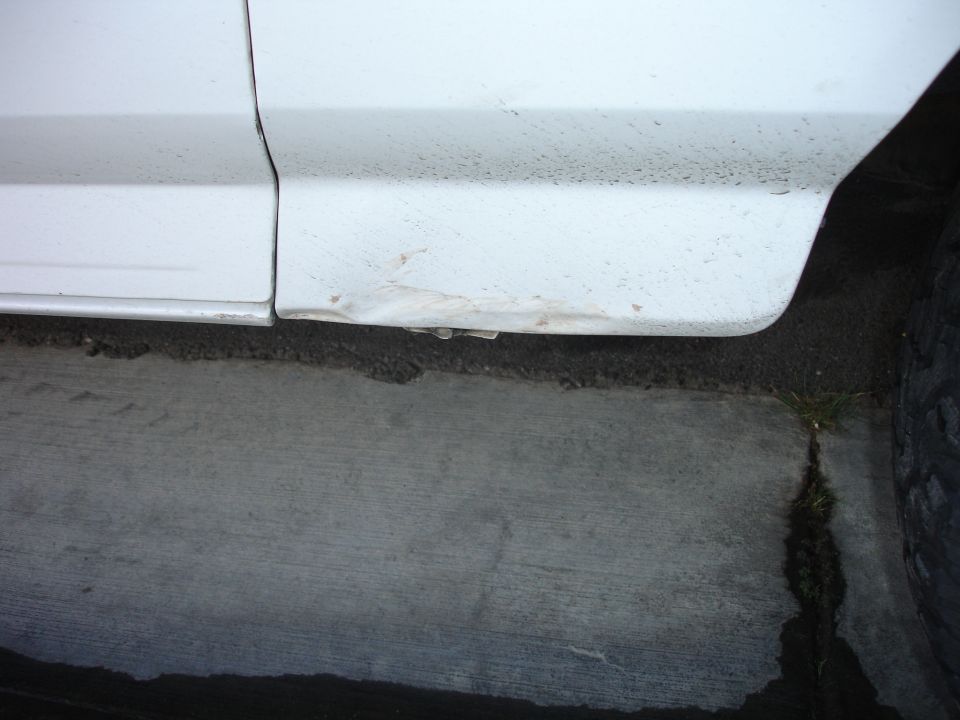 White vehicle lower body panel with dent and rust near the ground