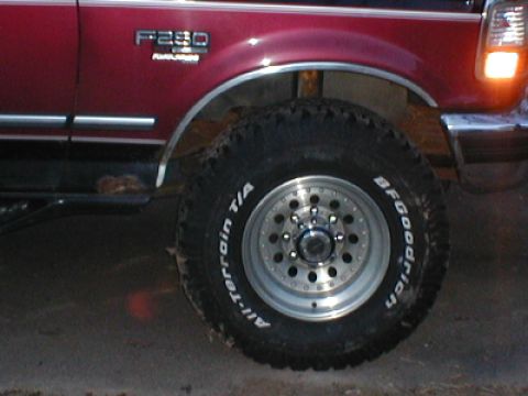 1979 Ford Bronco - A close-up shot focuses on the wheel and fender of a red Ford F-250 truck, highlighting its off-road tire.