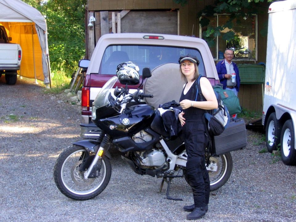 Rider standing beside a black BMW dual-sport motorcycle with side case on a gravel driveway