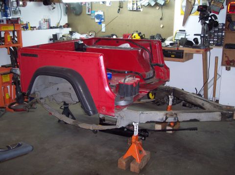 2003 Jeep TJ - The rear body of a red Jeep is elevated on jack stands, revealing its suspension and frame components.