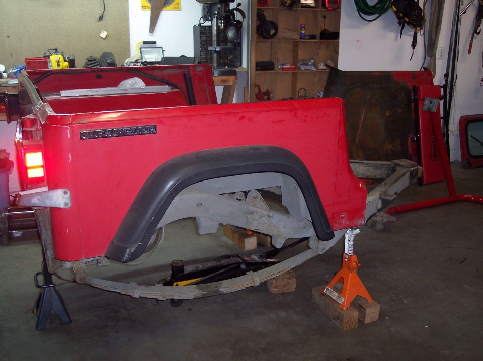 Red Jeep Wrangler rear body section on jack stands, showing leaf springs and frame