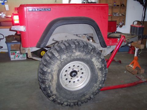 2003 Jeep TJ - Rear view of a red Jeep Wrangler showing the 'WRANGLER' badge and a large off-road tire, likely undergoing maintenance.