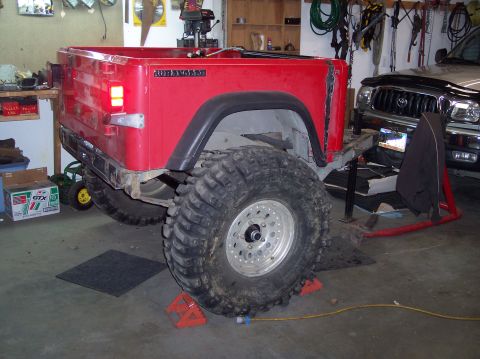 2003 Jeep TJ - Rear view of a red 2003 Jeep TJ Wrangler, modified with large tires and on jack stands in a garage.