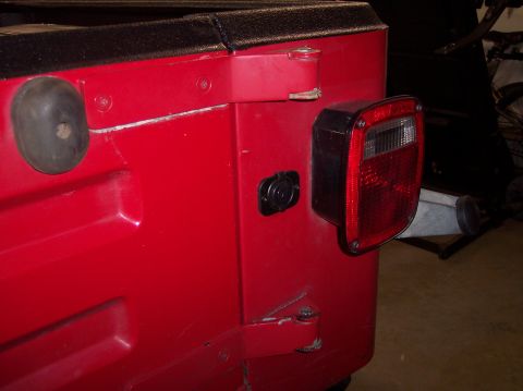 2003 Jeep TJ - Close-up of the rear corner of a red Jeep TJ, showing the taillight and trailer connection points.