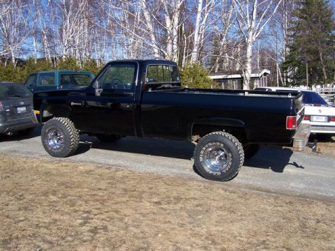 1996 Ford Bronco - A black pickup truck is parked outdoors with other vehicles nearby. The truck is seen from the side under a clear sky.