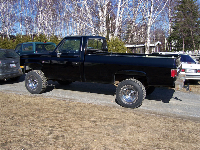 Black lifted square-body Chevy pickup, side view on gravel