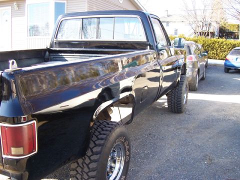 1996 Ford Bronco - A black pickup truck is parked on a gravel surface next to another vehicle.