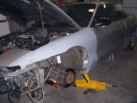 1996 Ford Probe - A silver car is being worked on in a garage, with its hood up and front fender removed.