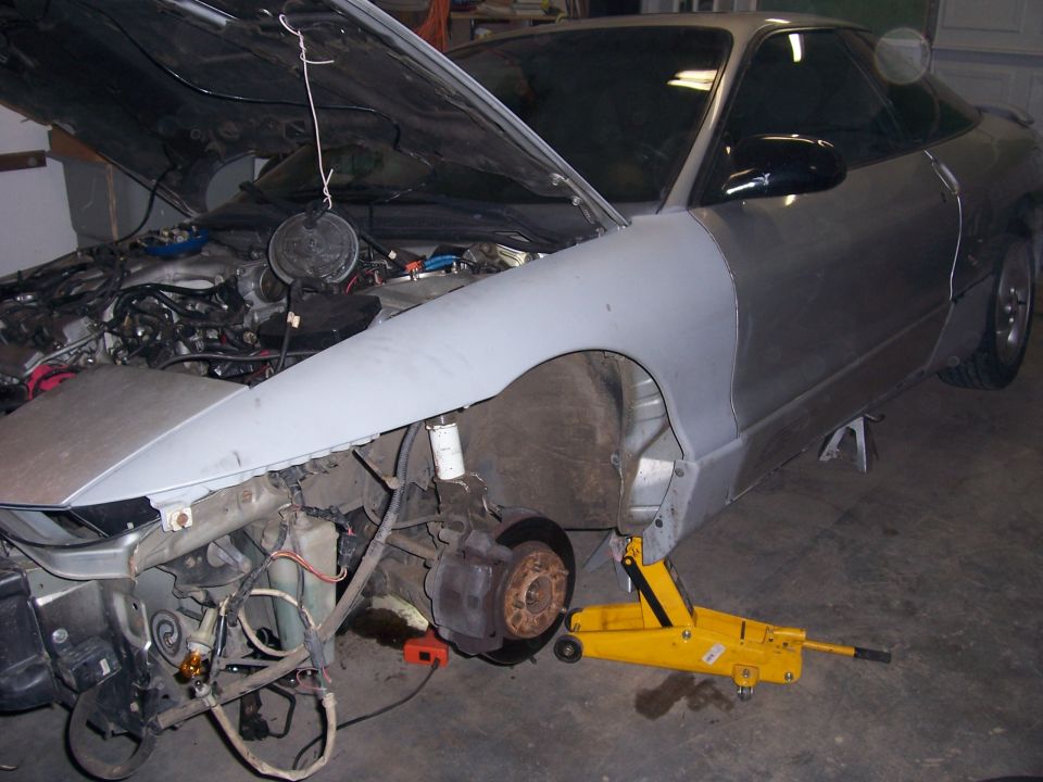 Silver car with hood open, undergoing repairs, front fender removed, on a yellow jack