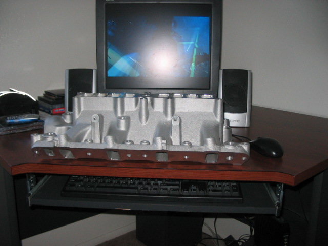 Aluminum intake manifold on a desk in front of a computer monitor and speakers