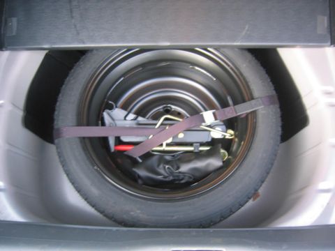 1993 Ford Probe - The spare tire and jack are secured with a strap in the trunk of a vehicle.