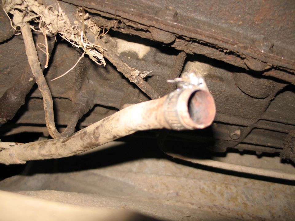 Rusty cut exhaust pipe end with band clamp under a dirty vehicle floor pan