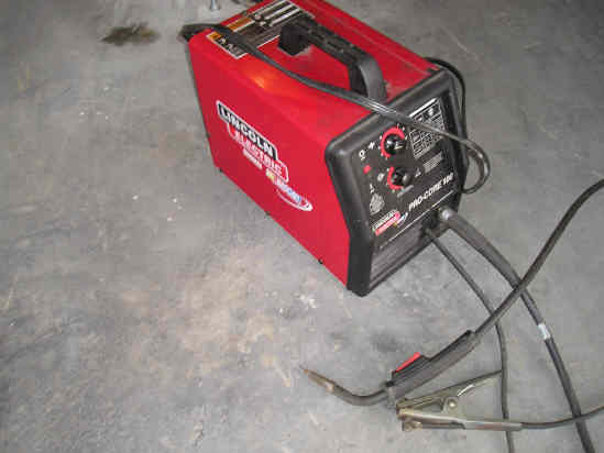 Red Lincoln Electric welder with black handle and cables on concrete floor