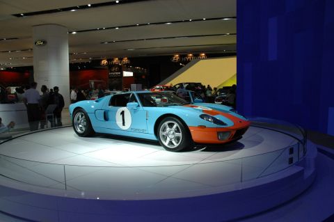 2005 Ford Mustang - A light blue and orange Ford GT race car is displayed on a rotating platform at an auto show.
