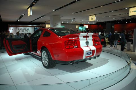 2005 Ford Mustang - A red Ford Shelby Mustang with white racing stripes is displayed with its driver's door open.