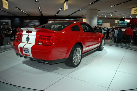 2005 Ford Mustang - Rear three-quarter view of a red 2005 Ford Mustang with white racing stripes on a display platform.