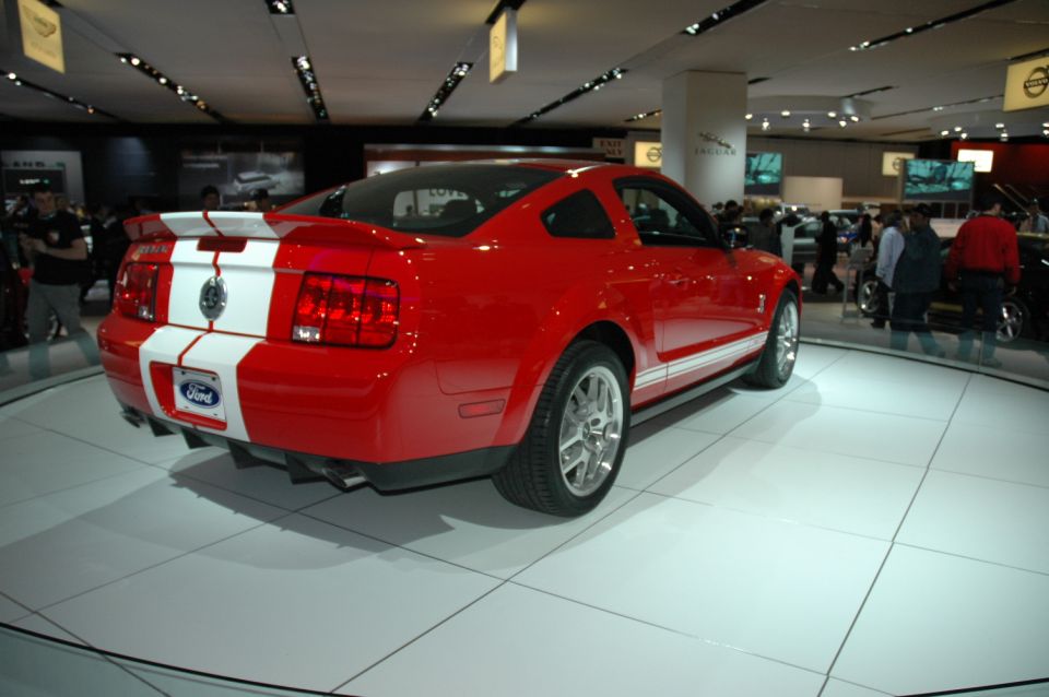 Red 2005 Ford Mustang with white racing stripes on a display turntable