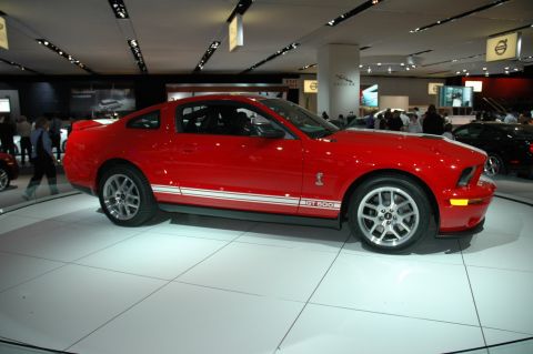 2005 Ford Mustang - A red 2005 Ford Mustang GT500 is showcased with its distinctive racing stripes and GT500 badging.