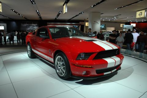 2005 Ford Mustang - Red 2005 Ford Mustang GT500 with white racing stripes displayed at an auto show.