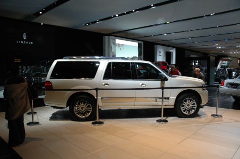2005 Ford Mustang - White Lincoln Navigator L on display at an auto show with other vehicles in the background.