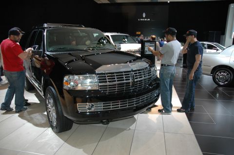 2005 Ford Mustang - A black Lincoln Navigator is showcased at an auto show with several onlookers.