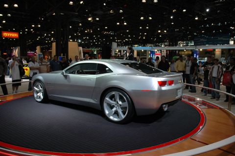 2005 Ford Mustang - A silver coupe is displayed on a turntable at an auto show, with spectators in the background.