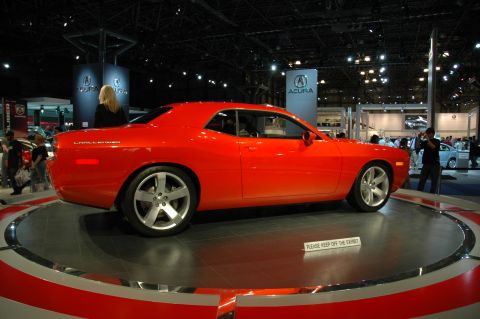 2005 Ford Mustang - Red Dodge Challenger on a rotating display at an auto show, with Acura signage in the background.