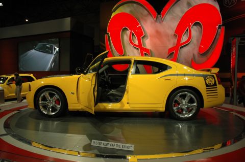 2005 Ford Mustang - A yellow 2007 Dodge Charger Super Bee is displayed with its doors open, a large Ram logo in the background.