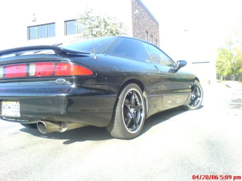 1997 Ford Probe - A black coupe with a spoiler and custom wheels is parked outdoors.