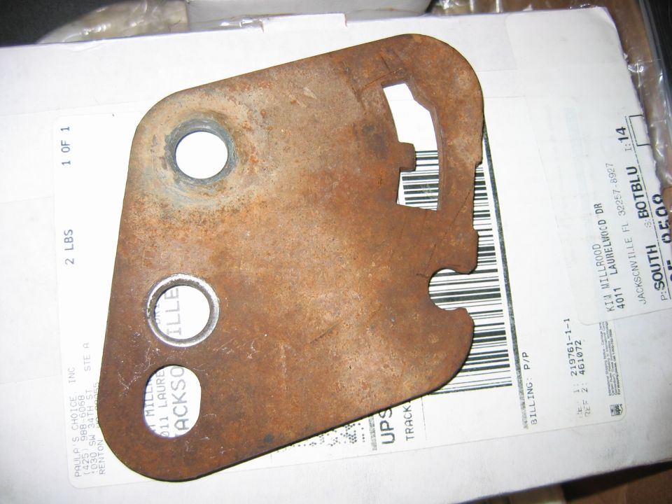 Rusty flat steel bracket with three bolt holes and notched edges lying on a UPS shipping box