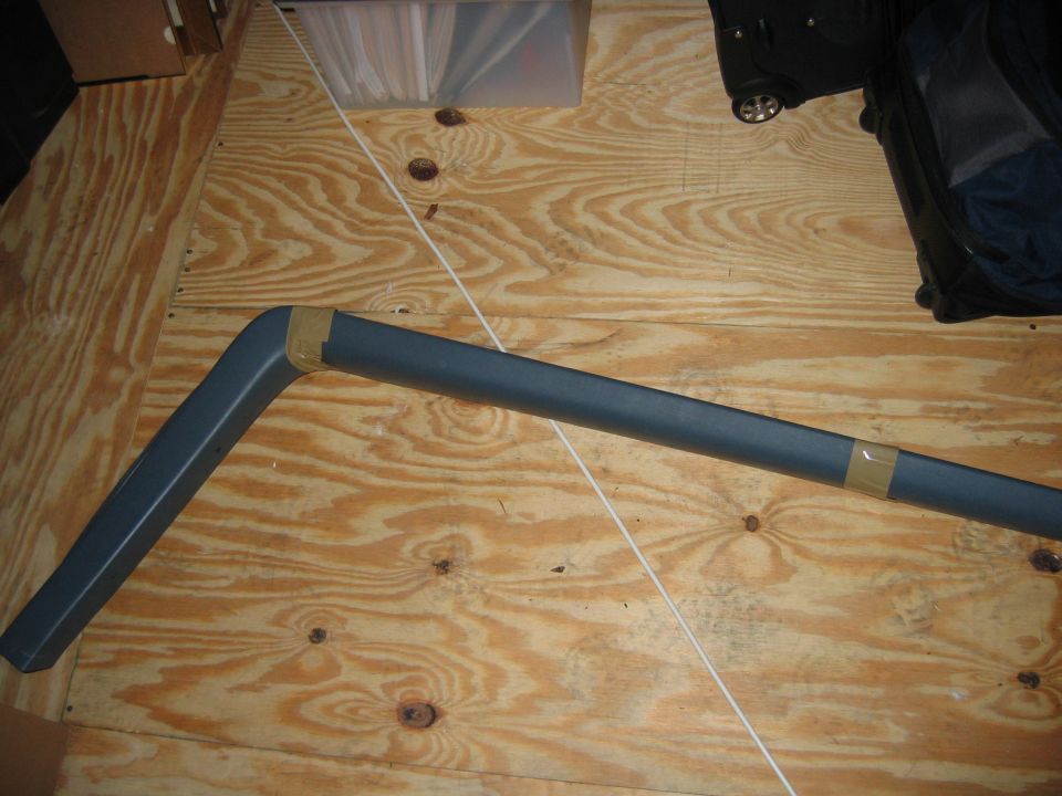 Dark gray plastic trim piece with taped joint, lying on plywood