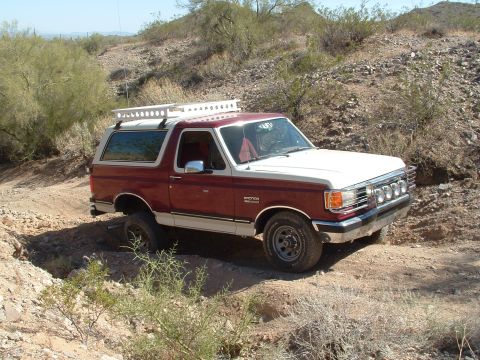 1990 Ford Bronco - This Ford Bronco is navigating a rough, off-road trail in a desert landscape.