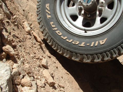 1990 Ford Bronco - A tire and wheel are visible in this close-up shot, surrounded by dirt and rocky terrain.