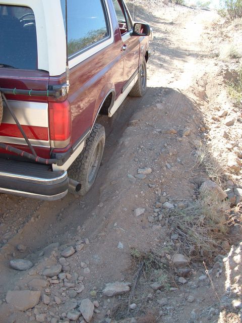 1990 Ford Bronco - A maroon and white Ford Bronco navigates a rocky dirt path, showing its side profile.