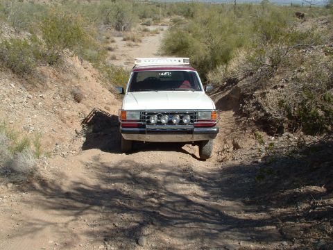 1990 Ford Bronco - This white and maroon SUV, likely from the 1990s, navigates a dusty, off-road trail.