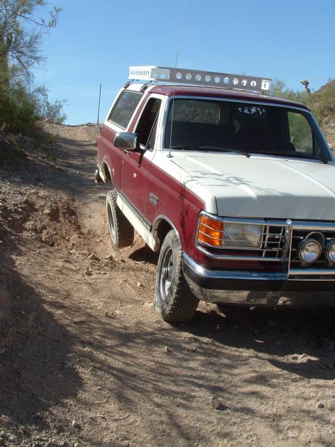 1990 Ford Bronco - This two-tone Ford Bronco navigates a dusty, off-road trail under a clear blue sky.