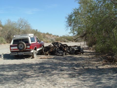 1990 Ford Bronco - A red and white SUV is parked next to a pile of burnt debris in a dry, brushy area.