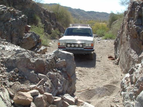 1990 Ford Bronco - White 1990 Ford Bronco navigates a narrow dirt path through a rocky canyon.