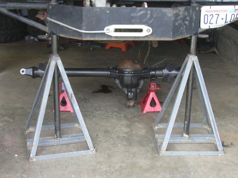 1991 Ford Bronco - The rear axle assembly of a vehicle is supported by jack stands, with a winch hook and license plate in view.