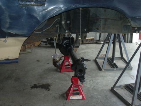 1991 Ford Bronco - Front axle assembly is supported by red jack stands, with a blue fender visible above.