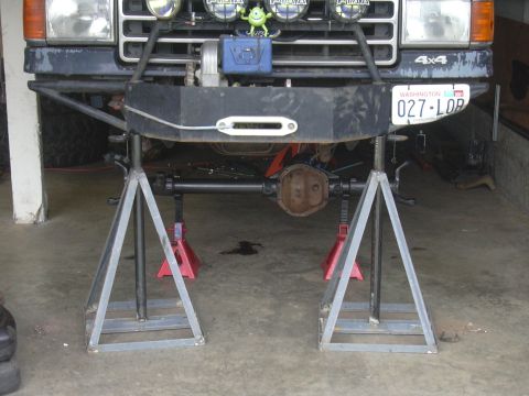 1991 Ford Bronco - The front of a 1991 Ford Bronco is raised on jack stands for maintenance, revealing its undercarriage and suspension components.