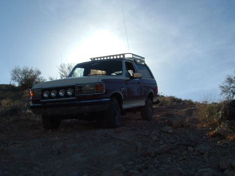 1990 Ford Bronco - A Ford Bronco is parked on a rocky incline under a bright, hazy sky.