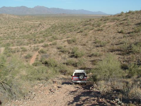 1990 Ford Bronco - Ford Bronco navigates a desert trail, mountains visible on the horizon.
