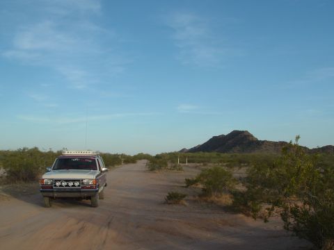 1990 Ford Bronco - A 1990 Ford Bronco drives down a dusty desert road under a clear blue sky.