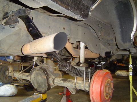 1989 Ford Bronco - Close-up view of the rear suspension and exhaust system of a vehicle undergoing maintenance.