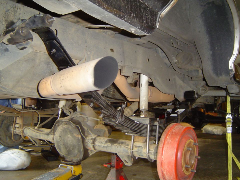 Underside of a truck on jack stands showing leaf-sprung rear axle, red brake drum and exhaust tip