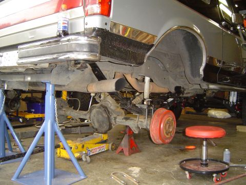 1989 Ford Bronco - The rear suspension of a truck is being worked on, supported by jack stands and a yellow floor jack.