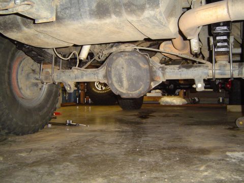 1989 Ford Bronco - Underside view of a vehicle's rear axle and leaf spring suspension system, with another vehicle partially visible in the background.